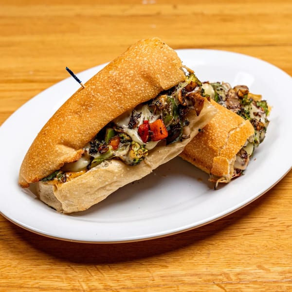 Two halves of a cheesy vegetable sub sandwich on a white plate, on a wooden table.