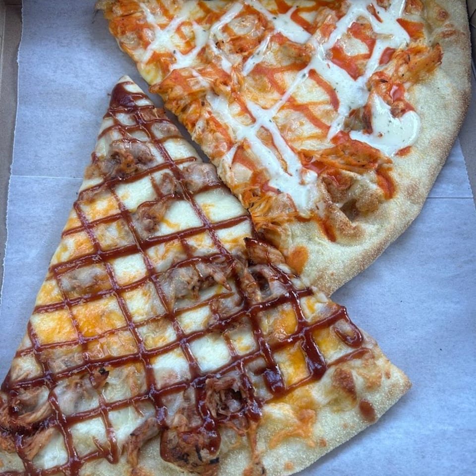 Two slices of Times Square Kitchen pizza, one buffalo chicken and one BBQ chicken, in a box.