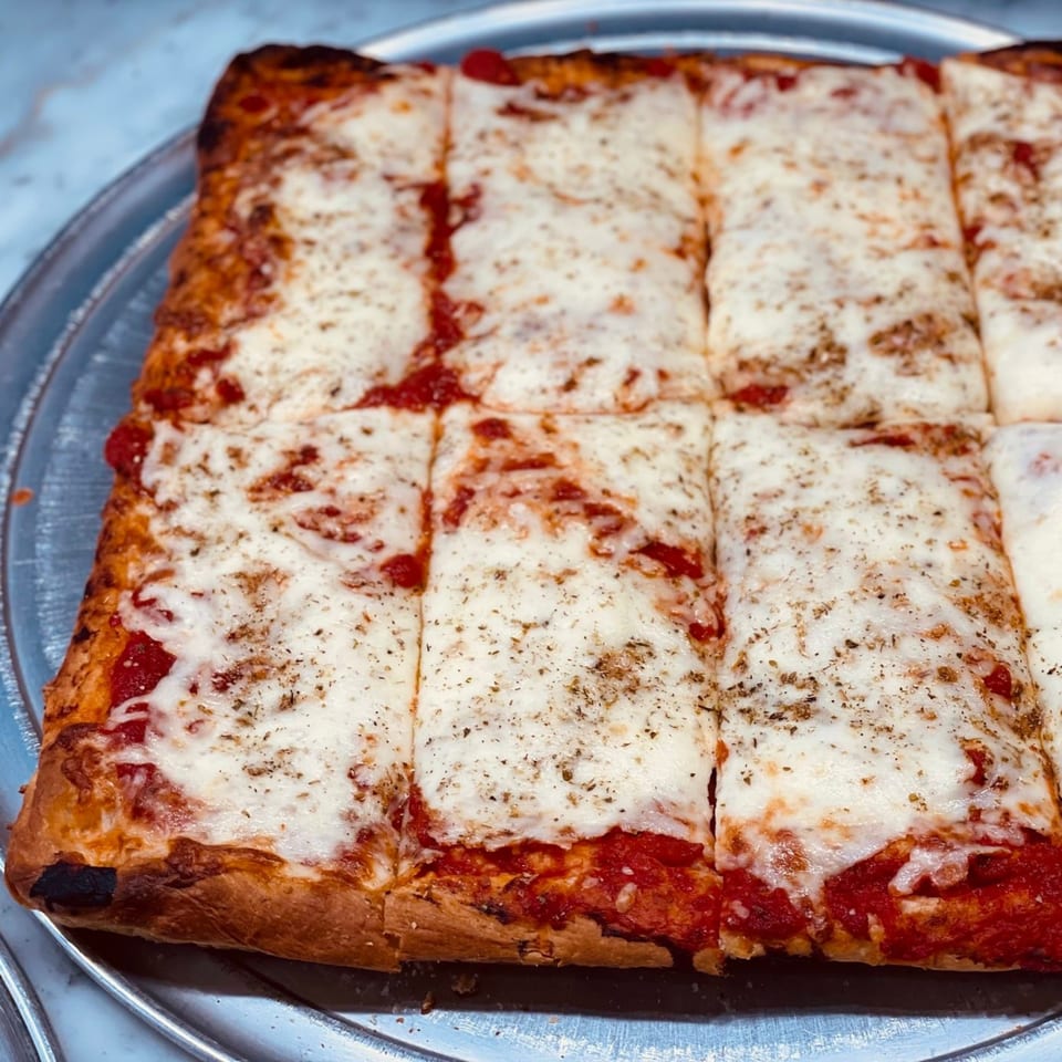 A rectangular Times Square Kitchen pizza, cut into squares, with melted cheese and tomato sauce.