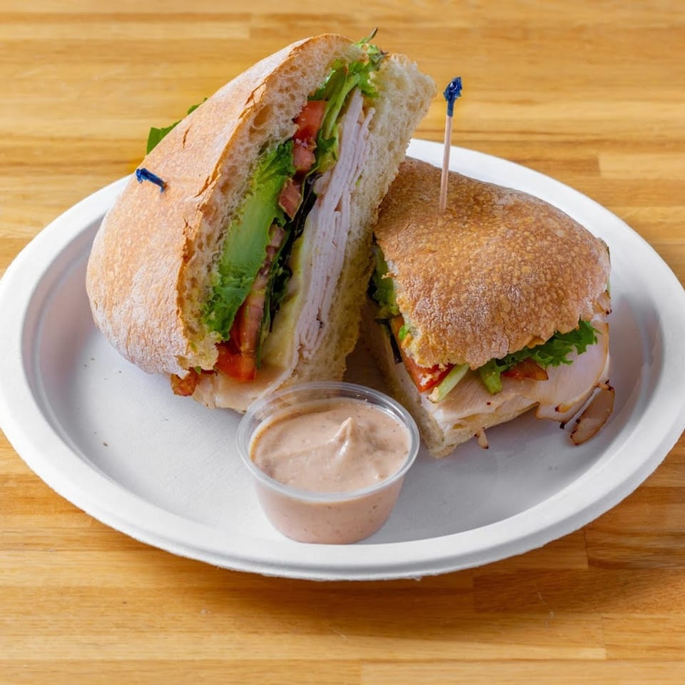 A turkey and avocado sandwich, cut in half, with a side of sauce on a white plate.